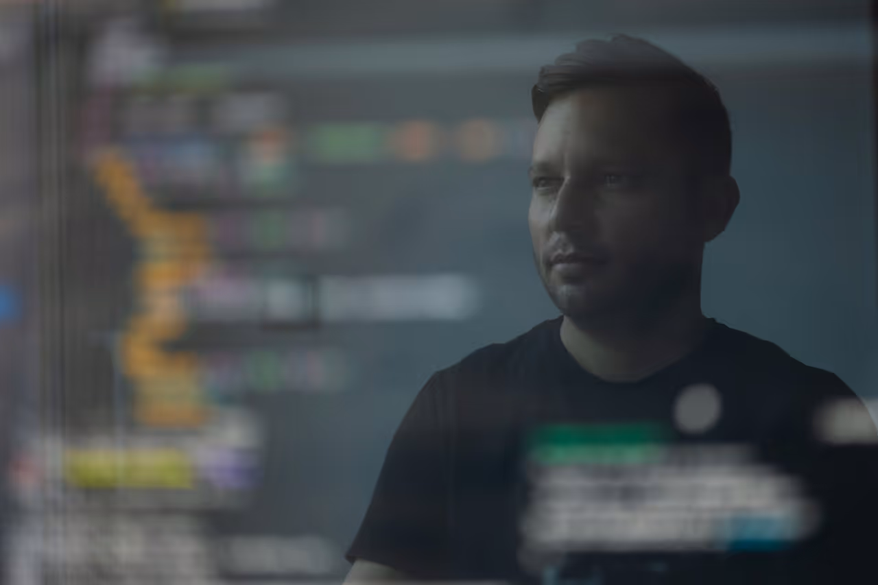 Man studying translucent display of colorful code, representing the human analysis guiding AlisAlpha’s transparent, rules-based AI workflows