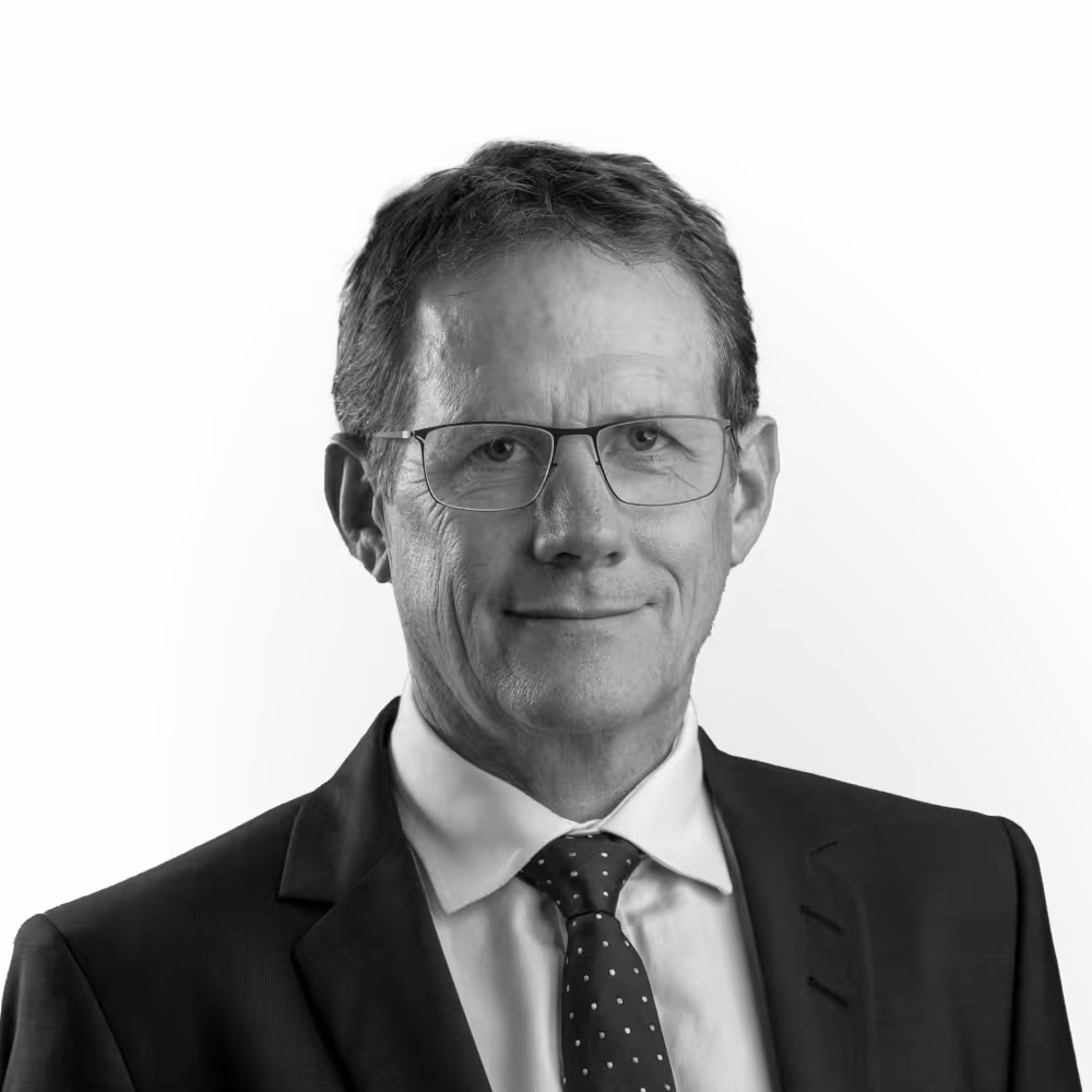 Portrait of a middle-aged man wearing glasses, a suit, white shirt, and patterned tie smiling slightly.